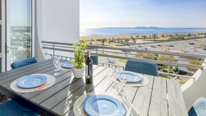 Un balcon avec une table dressée pour deux personnes, donnant sur une plage et un parking.