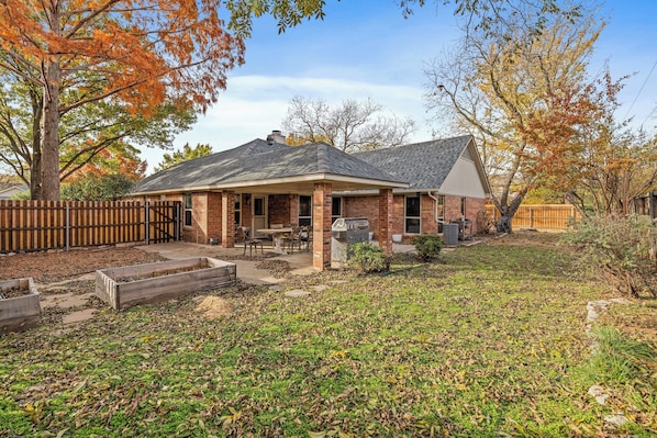 A two-story brick house with a covered patio, a fenced yard, and autumn foliage.