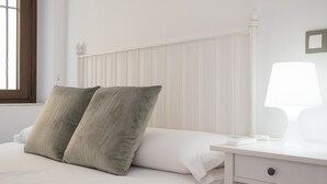 A bedroom with a bed, two pillows, a bedside table with a lamp, and a window with blinds.