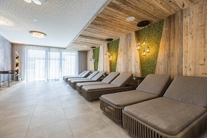 Relax in a serene spa area with lounge chairs, a textured green wall, and a large window.
