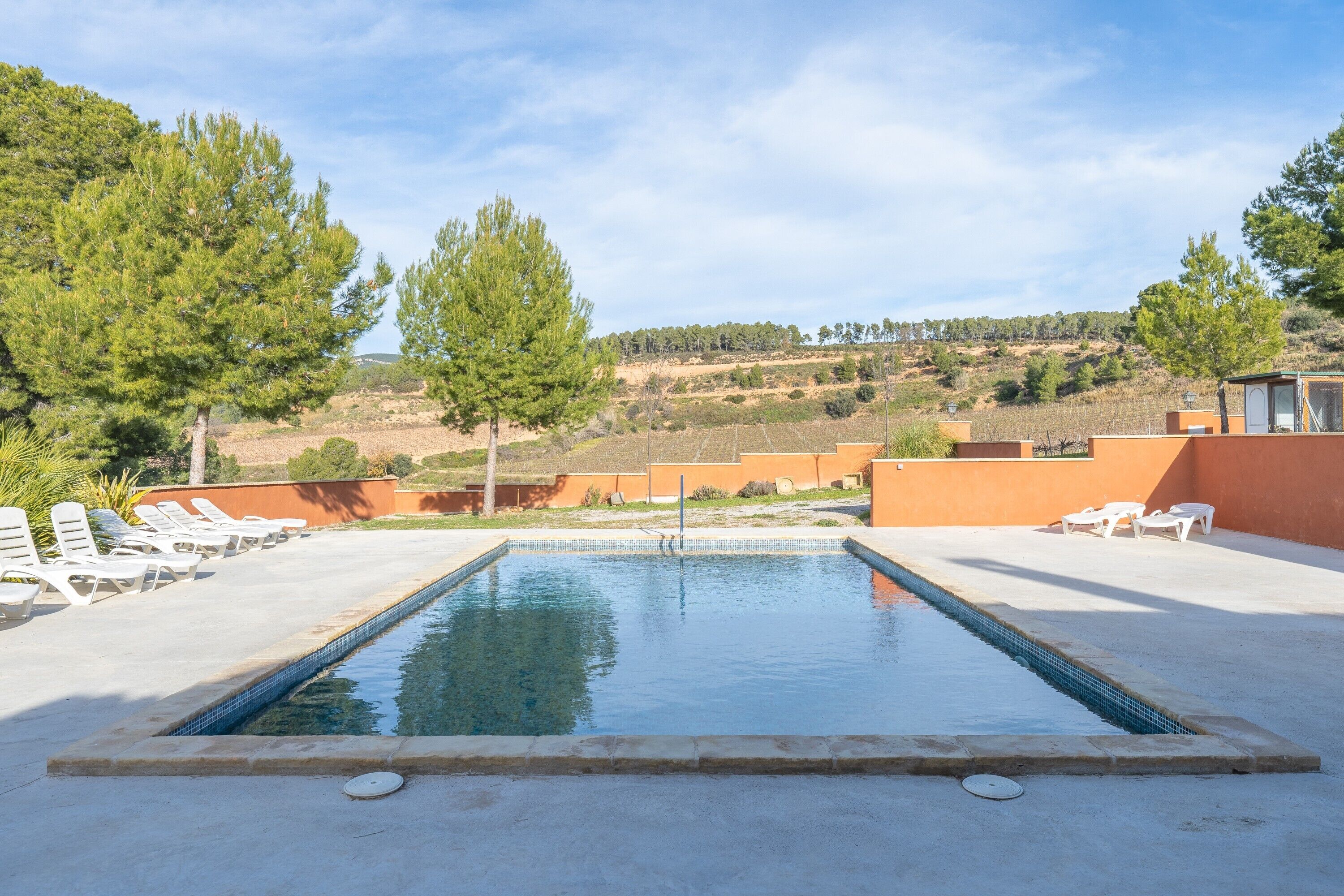 A rectangular pool with a tiled edge, surrounded by lounge chairs and a view of a hilly landscape.