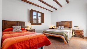 Une chambre avec deux lits, des têtes de lit en bois, une fenêtre, des tables de chevet avec des lampes et un sol carrelé.