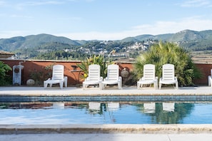 A pool with white lounge chairs, a tiled edge, and a view of mountains and houses in the background. - Rural House 'Ca La Munda-Can Cruset' with Mountain Views, Private Pool & Wi-Fi (Torrelles de Foix)