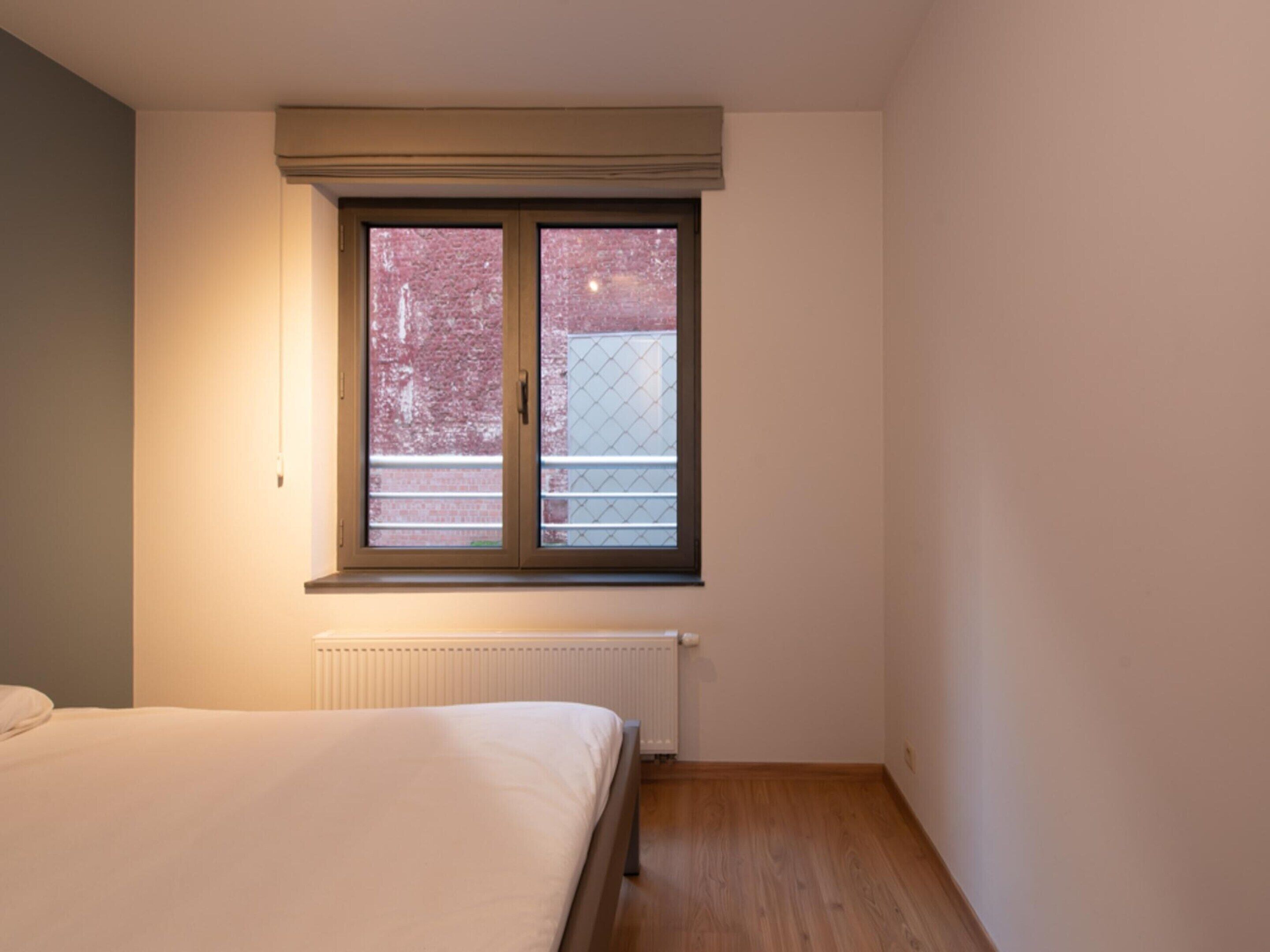 A bedroom with a single bed, a window with a view of a building, and a radiator below the window.