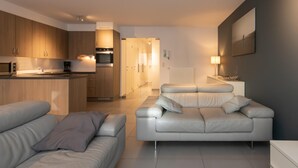 A modern living room with a sofa and a dining area with wooden cabinets and a built-in oven. - Apartment in Ostend Near the Seafront (Ostend)