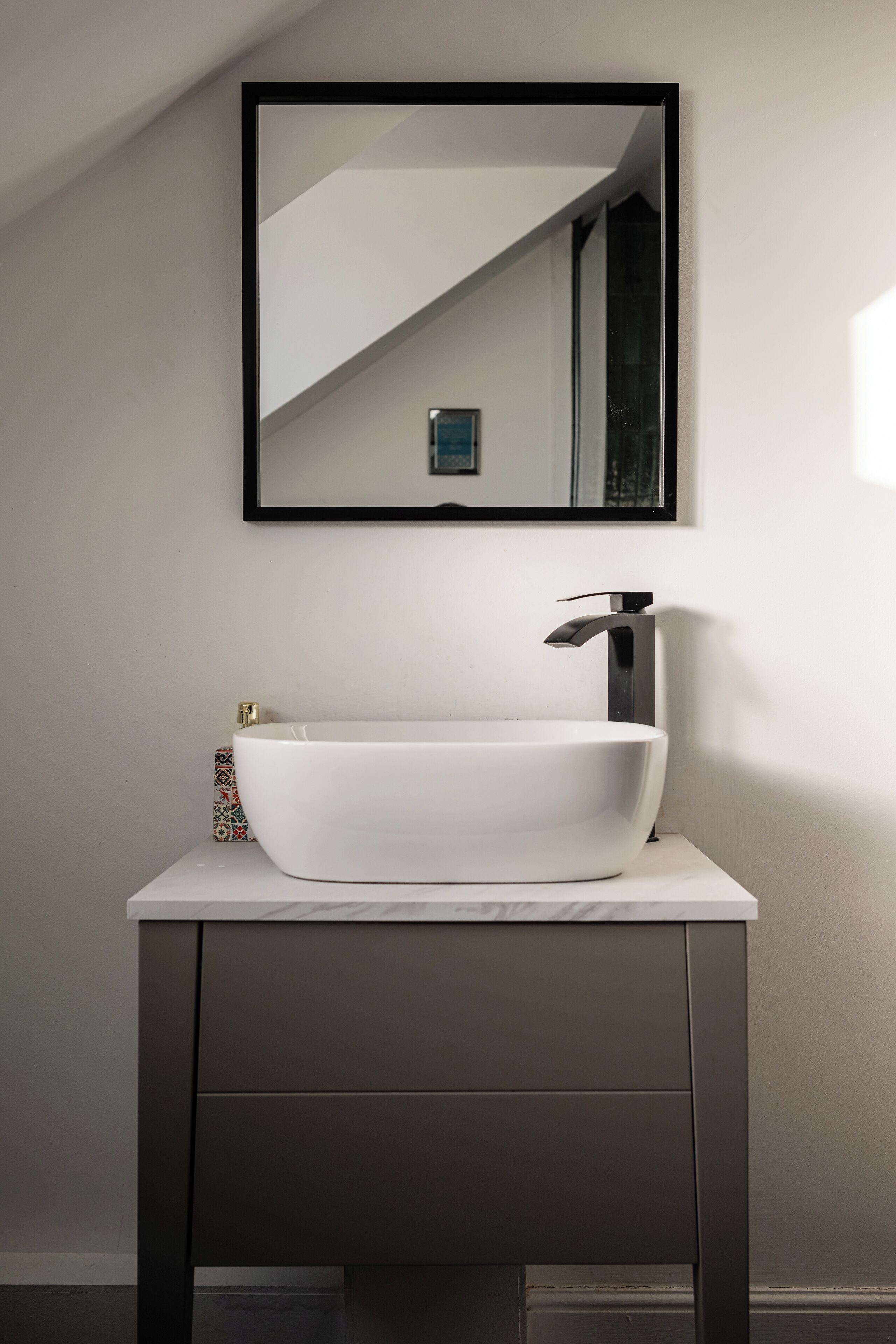 A modern bathroom with a white vessel sink, a dark vanity, and a mirror above the sink.