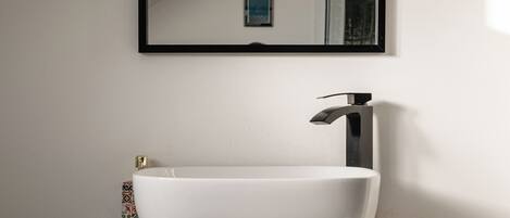 A modern bathroom with a white vessel sink, a dark vanity, and a mirror above the sink.