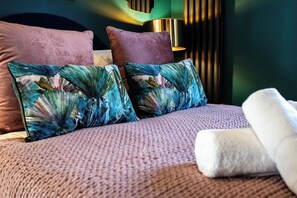 Ein Bett mit zwei Zierkissen, einer strukturierten Decke und einem aufgerollten weißen Handtuch.