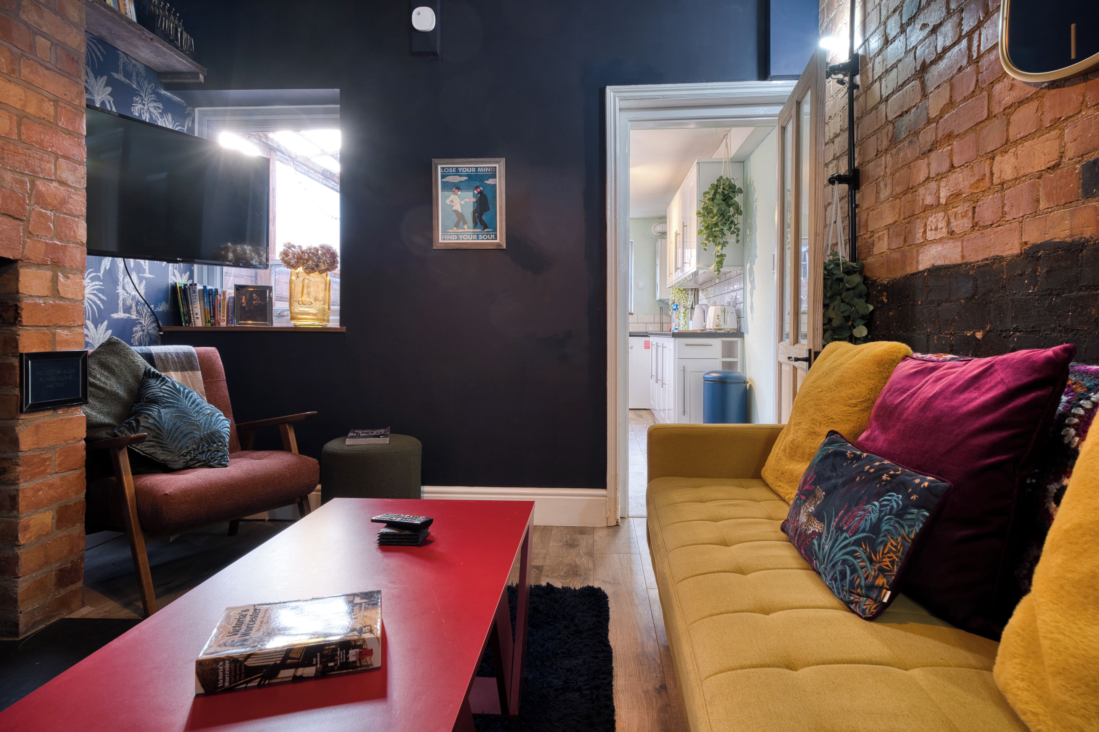 A cozy living room with a red table, yellow sofa, and a brick wall.