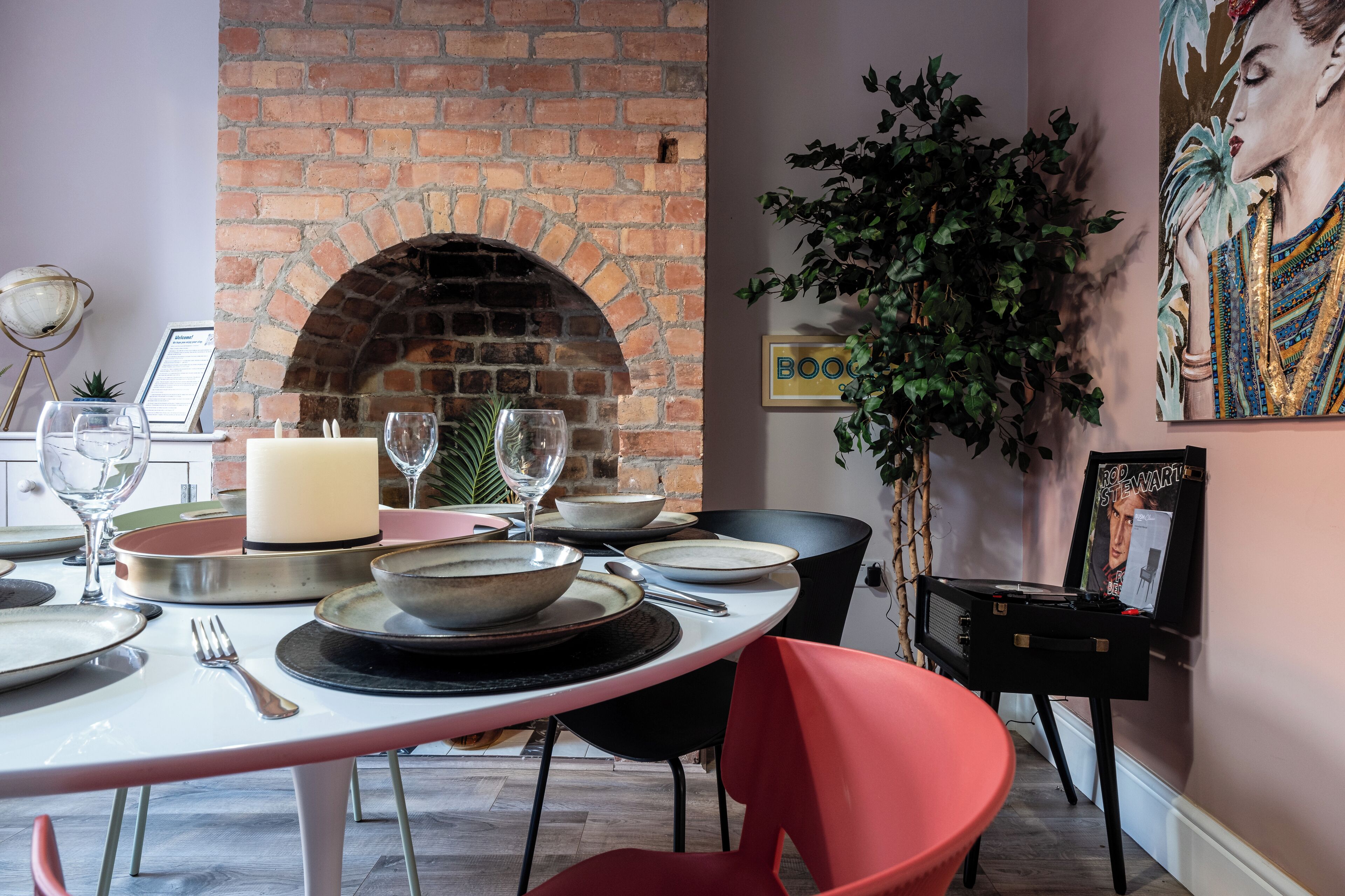 Un comedor con chimenea de ladrillo, una mesa dispuesta para cuatro personas y una planta grande en maceta.