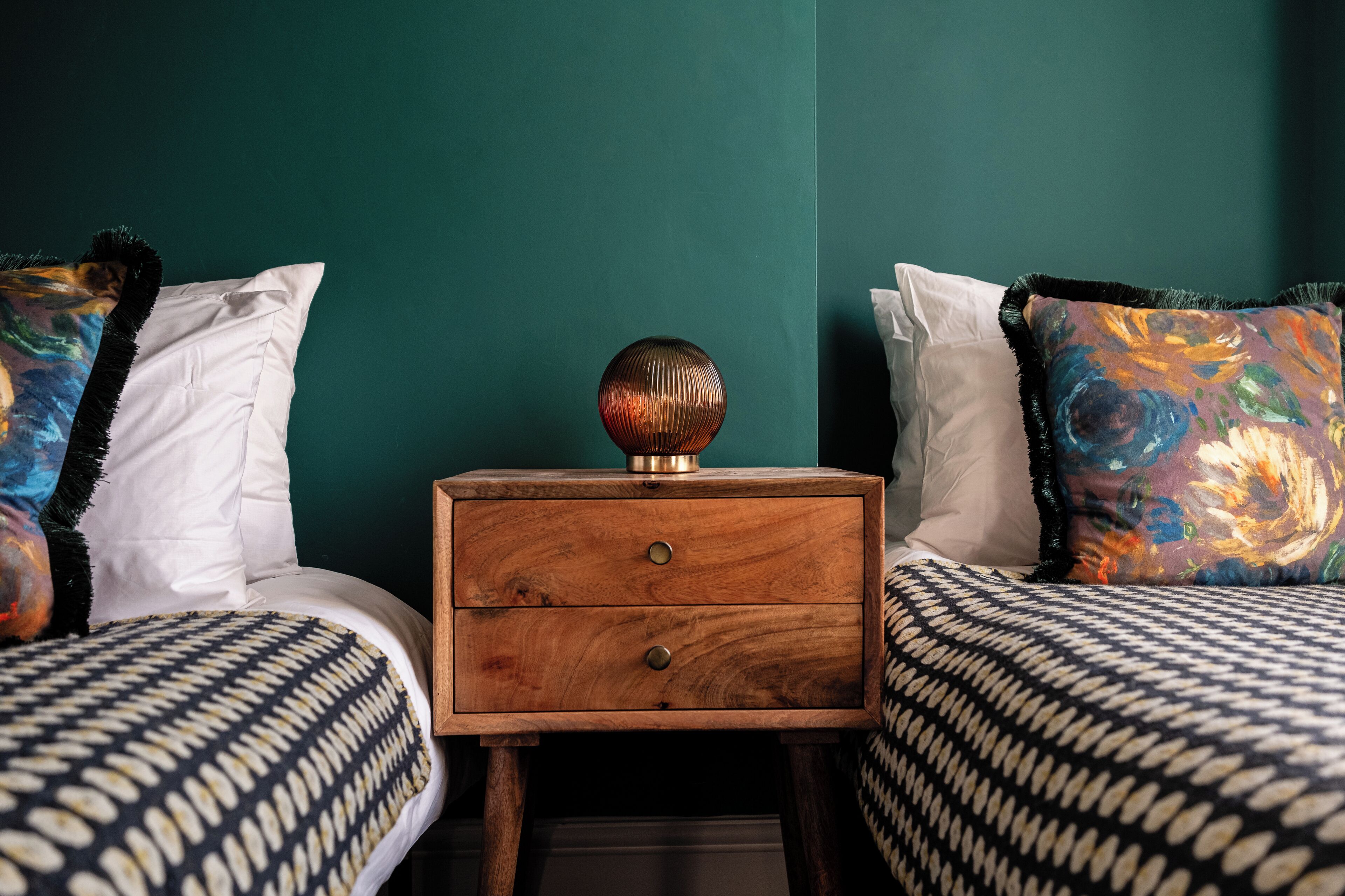A bedroom with two beds, a wooden nightstand, and a teal wall.
