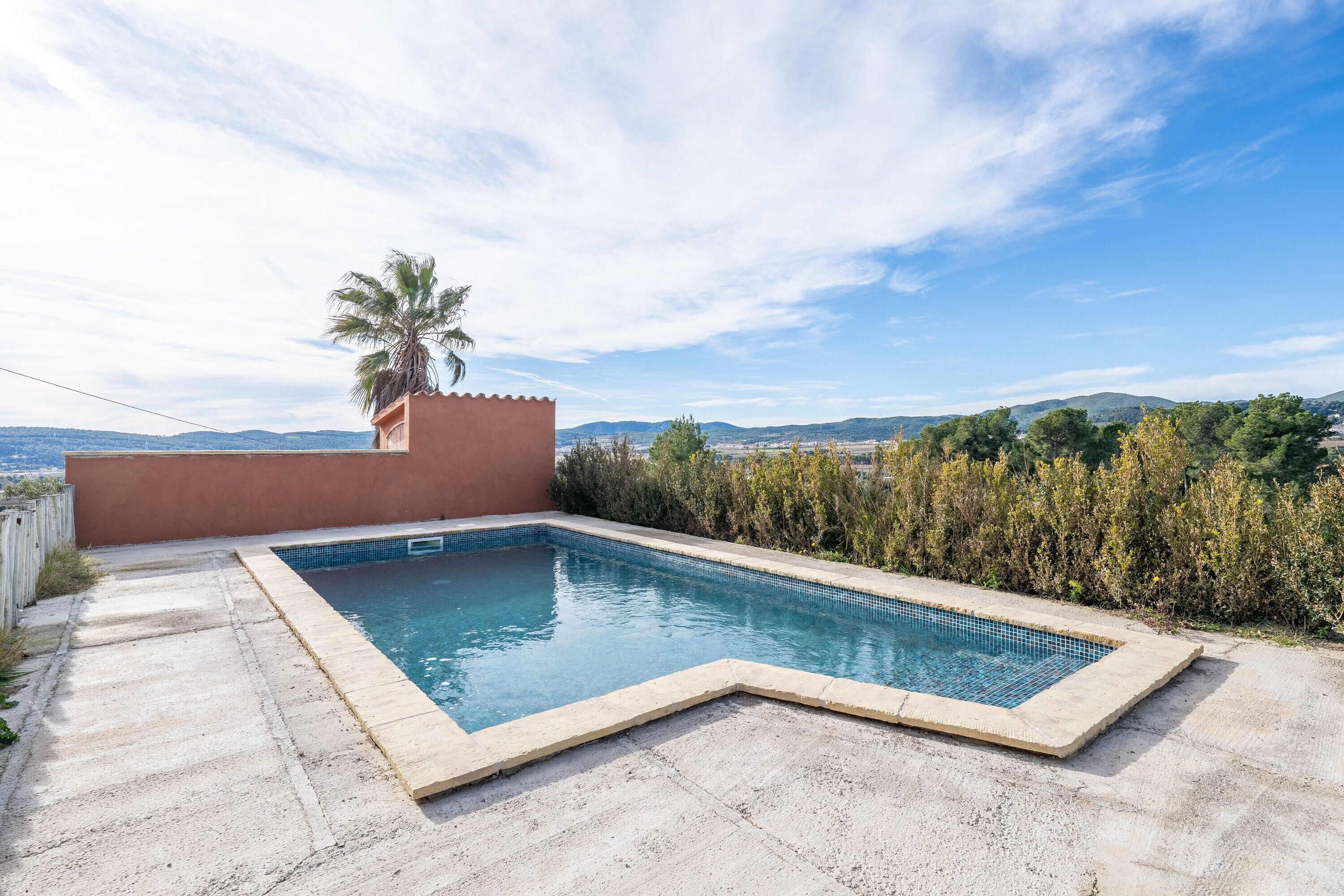 A rectangular swimming pool with a tiled edge, surrounded by a concrete deck and a low wall.