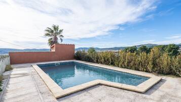 A rectangular swimming pool with a tiled edge, surrounded by a concrete deck and a low wall.