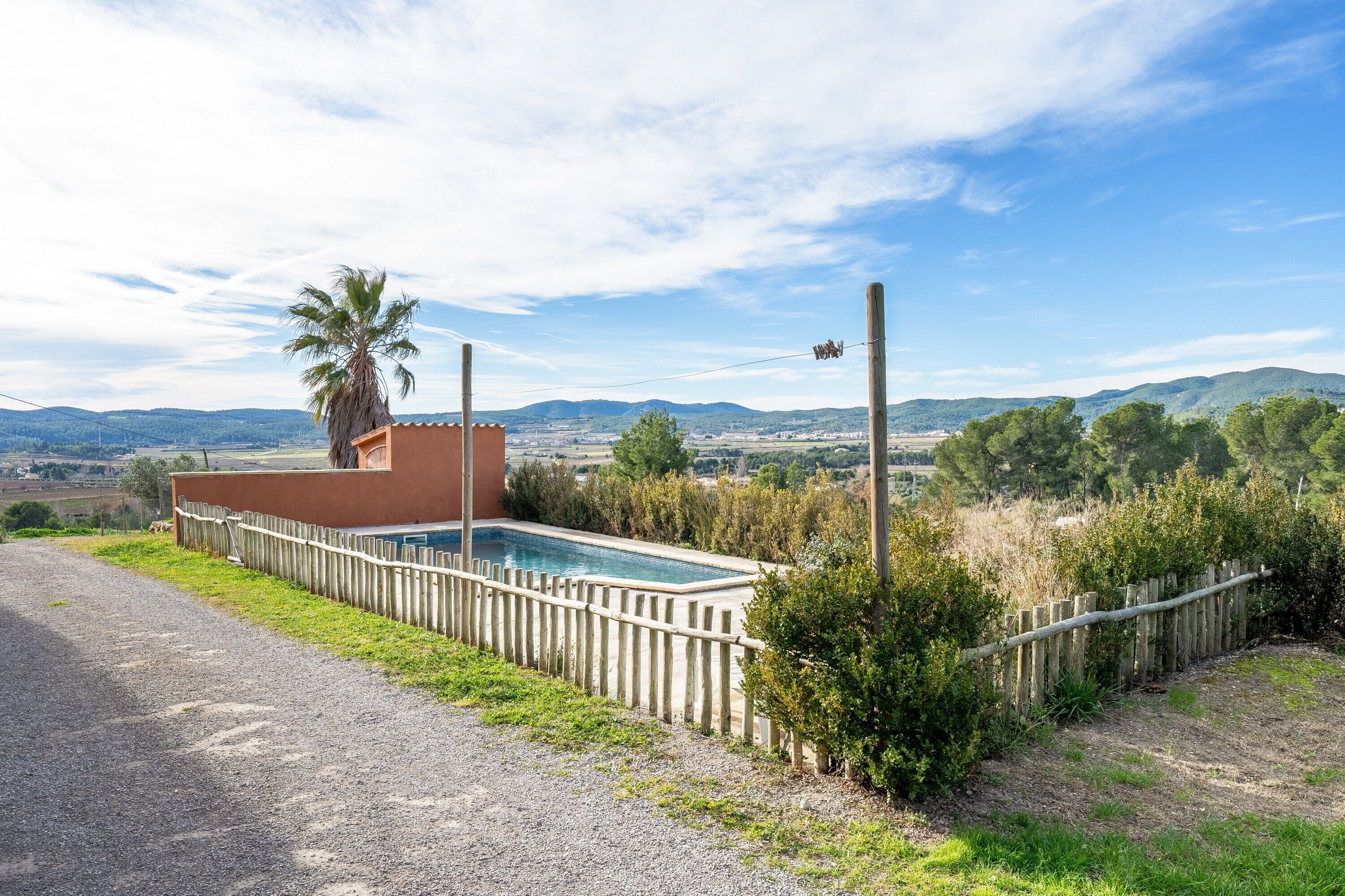 Ein Pool mit Holzzaun, einer Palme und Blick auf ferne Hügel.