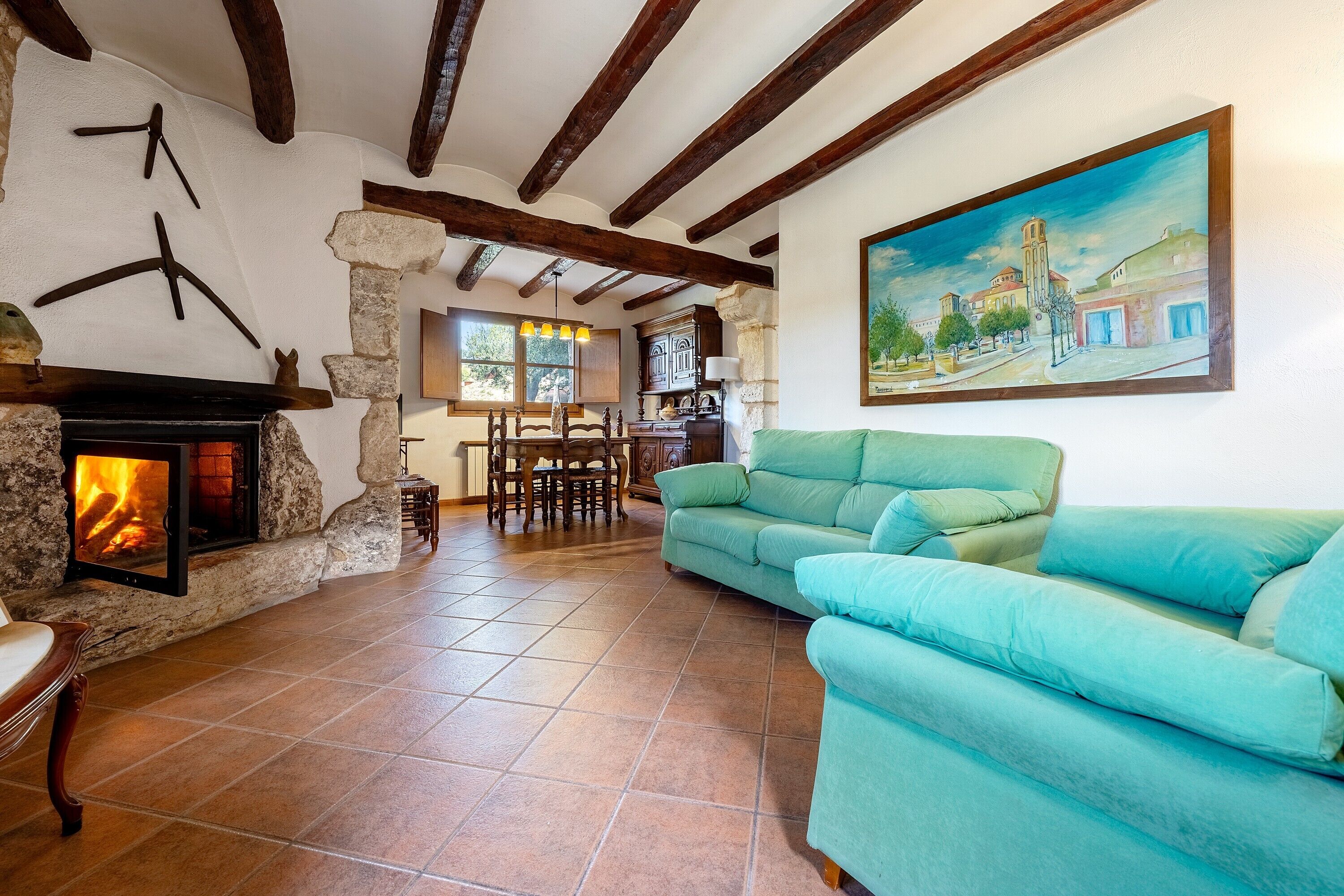 Un salon avec une cheminée, un canapé vert, une table à manger avec des chaises et un tableau accroché au mur.
