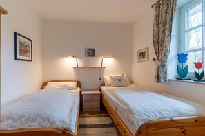 Een slaapkamer met twee eenpersoonsbedden, een nachtkastje, een wandlamp en een raam met gordijnen.