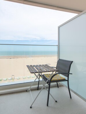 Un balcón con vista a la playa, una mesa de metal y una silla con cojín.