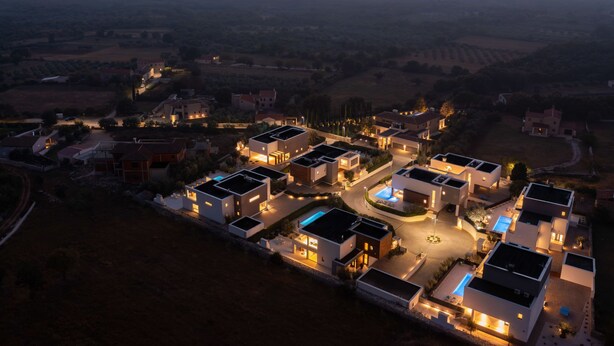 Een modern woongebied met eigentijdse huizen, een centraal gelegen zwembad en uitzicht op het omliggende landschap tijdens de schemering.