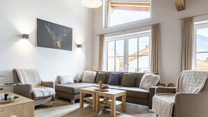 Ett mysigt vardagsrum med en soffa, fåtöljer, ett soffbord och en tavla med en hjort på väggen.