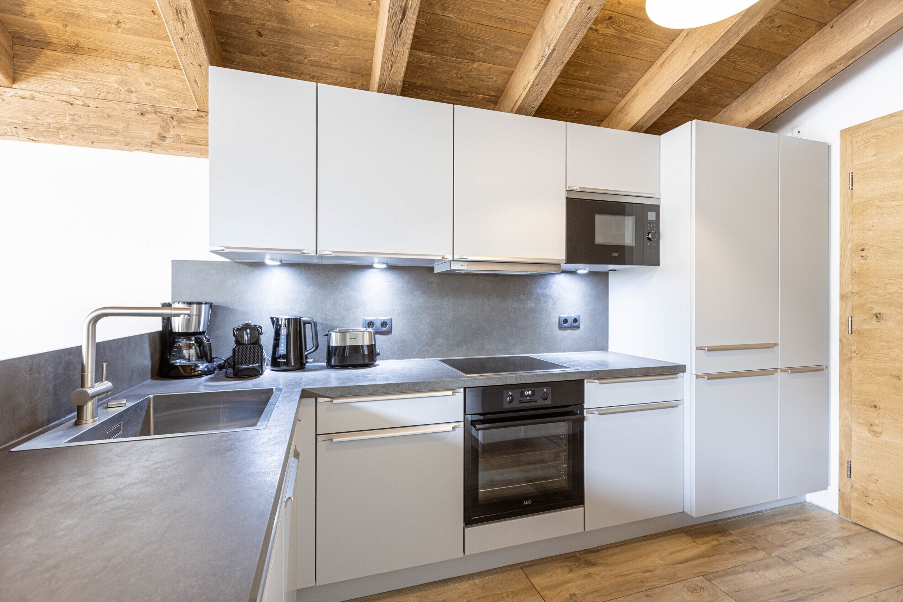 A modern kitchen with white cabinets, stainless steel appliances, and a wooden ceiling.