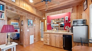 A cozy cabin-style kitchen with wooden walls, a red accent wall, and a modern refrigerator.