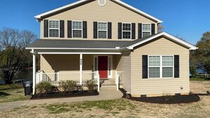 A two-story house with a front porch, a red door, and a small attached garage. - Spacious 5-bedroom lakefront house in Anderson, 13 miles to Clemson (Anderson)