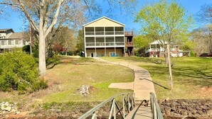 A wooden bridge leading to a building with a balcony, surrounded by trees and a grassy area. - Spacious 5-bedroom lakefront house in Anderson, 13 miles to Clemson (Anderson)