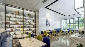 A modern dining area with marble flooring, blue and green chairs, and a variety of books and decorative items on shelves. - FuShang Hotel (Foshan)