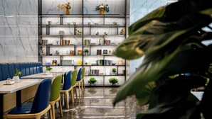 A modern library with marble walls, a bookshelf filled with books and decorative items, and a seating area with blue and green chairs. - FuShang Hotel (Foshan)