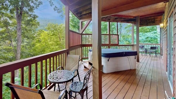 A covered outdoor deck with a hot tub, a table, and chairs. - Expansive home with arcade game, pool table, & Great Smoky Mountains view (Gatlinburg)