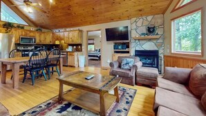 A spacious living area with a wooden ceiling, a stone fireplace, a television, and a cozy seating arrangement. - Expansive home with arcade game, pool table, & Great Smoky Mountains view (Gatlinburg)