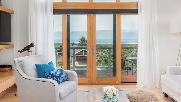 Ein modernes Wohnzimmer mit einem großen Schiebeglasfenster, das auf einen Balkon mit schöner Aussicht führt.