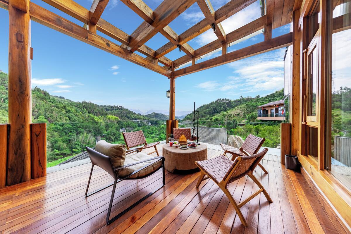 A wooden deck with a round table and chairs, overlooking a lush green landscape.