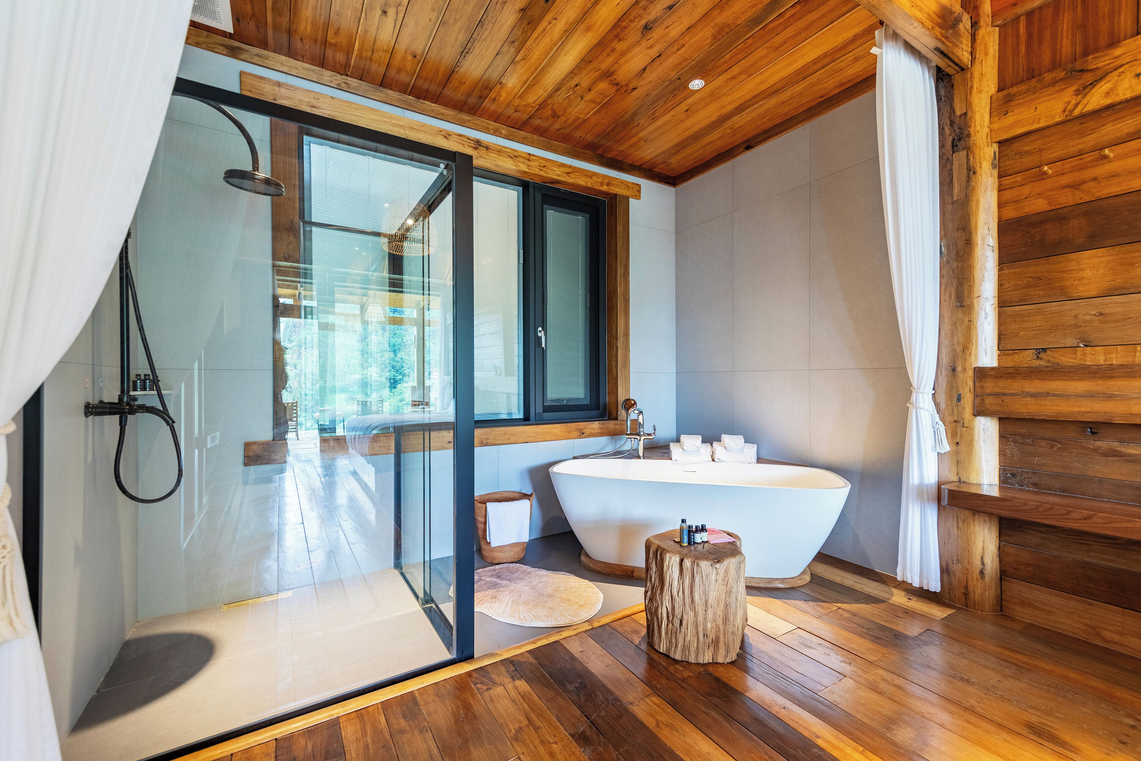 Ein modernes Badezimmer mit einer gläsernen Duschkabine, einer freistehenden Badewanne und Holzboden.