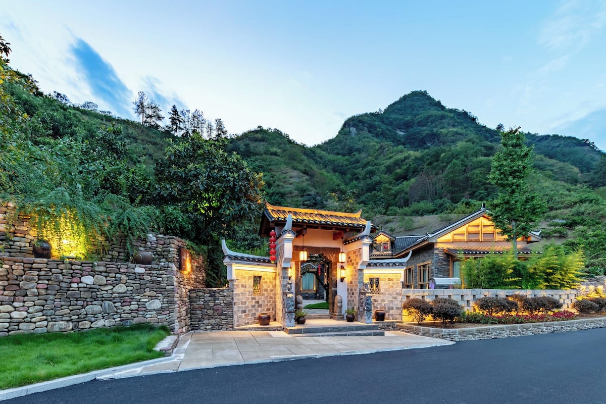 A traditional-style building with a stone entrance, surrounded by lush greenery and hills.