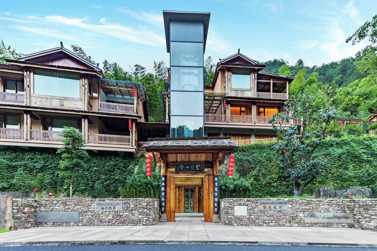 A traditional wooden building with a central entrance, balconies, and a stone wall.