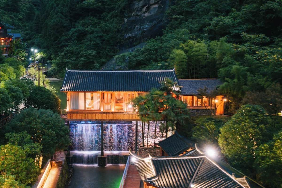 A traditional building with a tiled roof, a waterfall, and a surrounding lush garden.