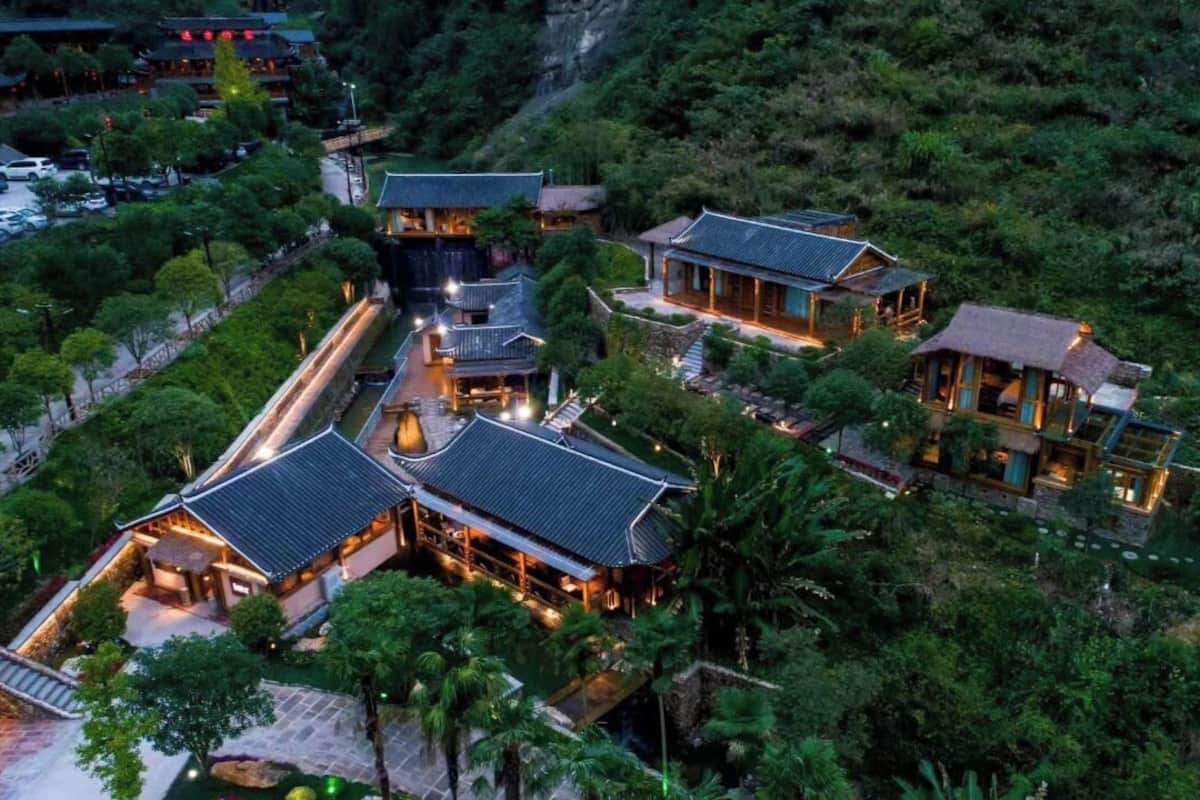 A traditional-style hotel with multiple buildings, a well-maintained garden, and a mountainous backdrop.