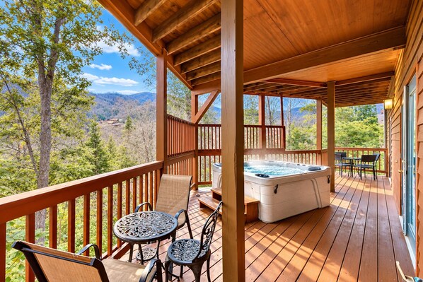 A wooden deck with a hot tub, outdoor seating, and a scenic mountain view.