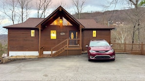 A wooden cabin with a welcoming sign, a staircase, and a parked car in front.