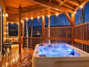 Una terraza de madera con un jacuzzi, luces colgantes y un banco.