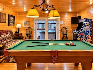 Un interior de madera con mesa de billar, dos sillas, un sofá y un televisor.