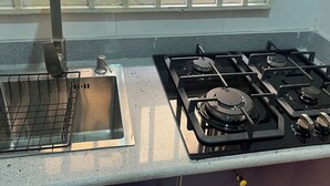 A kitchen with a gas stove, a sink, and a window with a patterned curtain. - Private, Cozy, CityCentre Studio Apartment in the heart of Abuja (Abuja)