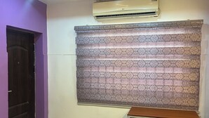 A room with a purple wall, a patterned curtain, an air conditioning unit, a wooden desk, and a trash bin. - Private, Cozy, CityCentre Studio Apartment in the heart of Abuja (Abuja)