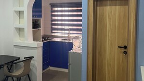 Een kleine kamer met kitchenette, een bed en een deur.