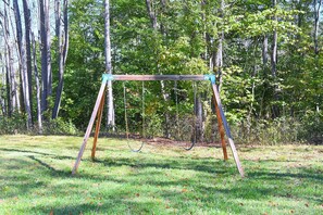 Une balançoire installée dans un espace herbeux, avec des arbres en arrière-plan.