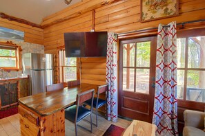 A cabin interior with a wooden interior, a dining table, chairs, a refrigerator, and a television mounted on the wall.