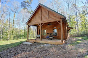 A wooden cabin with a porch, a dining table, and chairs.