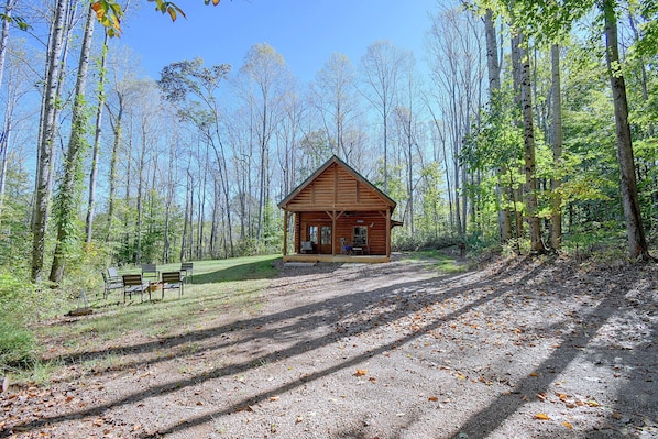 Une cabane dotée d’un porche et d’un espace salon, entourée d’une forêt.