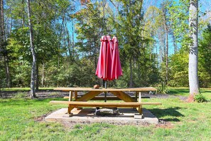 A picnic table with a red umbrella in a park.